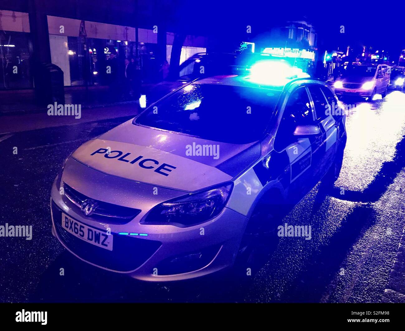 Police car parked on a city street at night with blue lights flashing Stock Photo