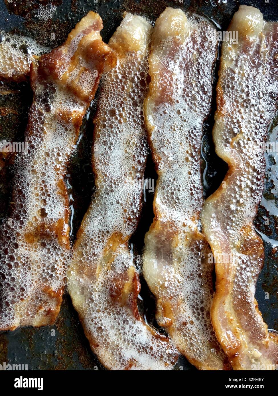 Four slices of bacon in a frying pan - Smartphone Captured Stock Image