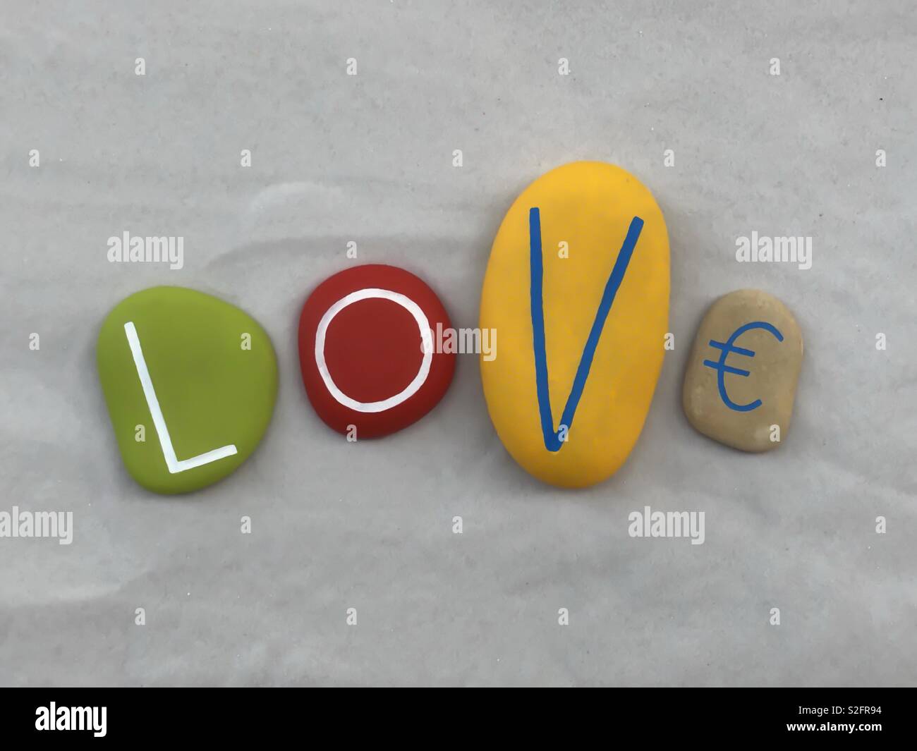 Love and money, conceptual composition with painted stones over white sand Stock Photo