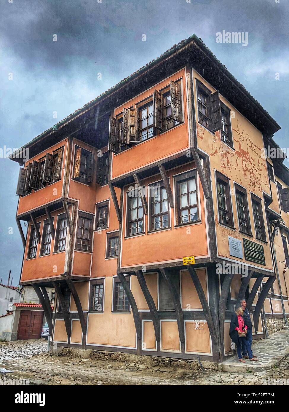 A couple escapes the rain by standing under a protected section of an historical building in Plovdiv, Bulgaria. - Smartphone Captured Stock Image