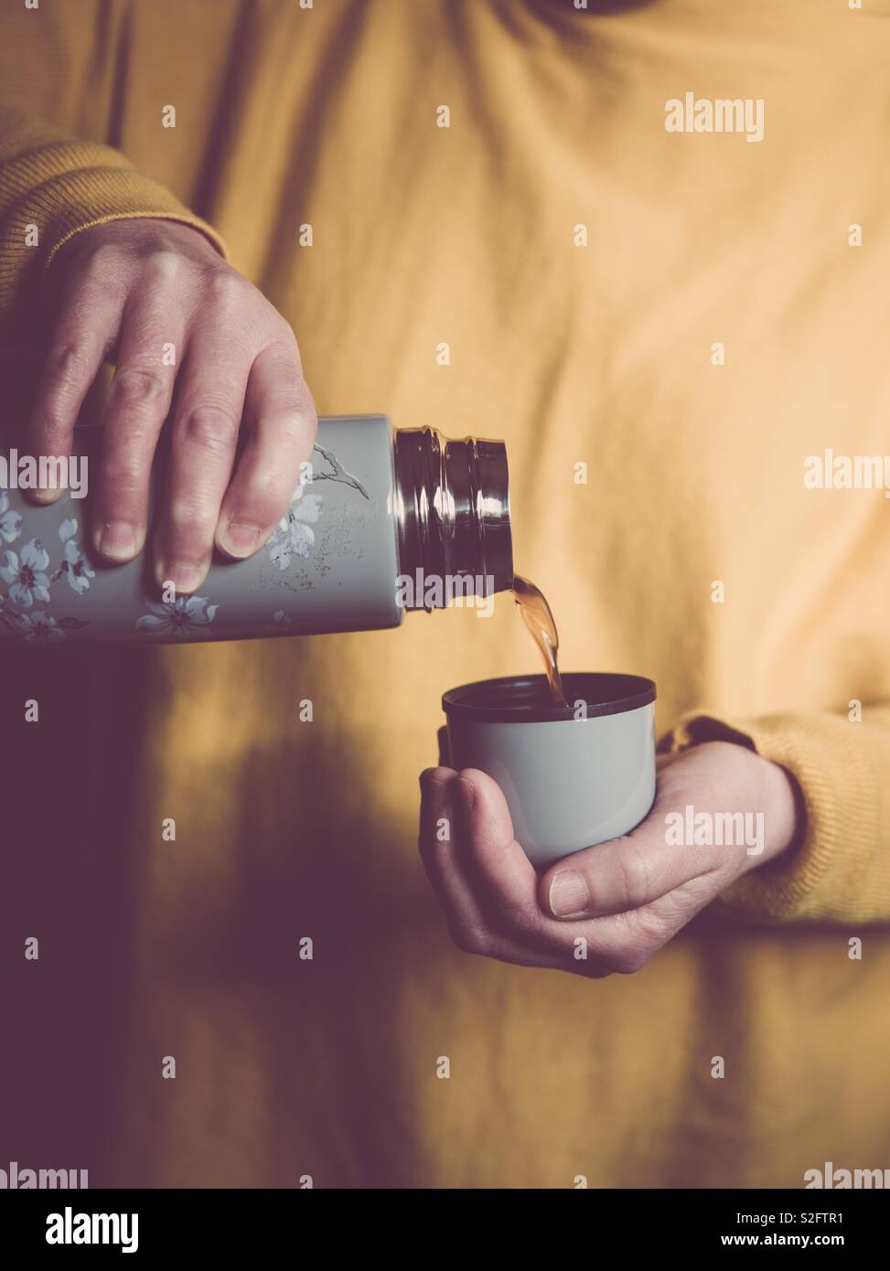A mid section of a girl wearing yellow clothes and pouring hot coffee or tea from a thermos flask - Smartphone Captured Stock Image
