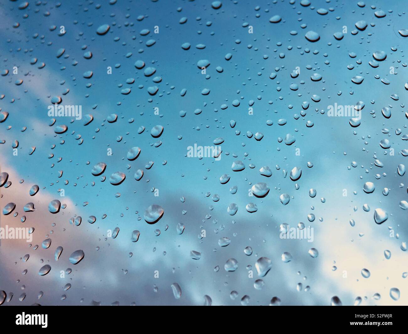 Raindrops on window pane with blue sky in background Stock Photo - Alamy