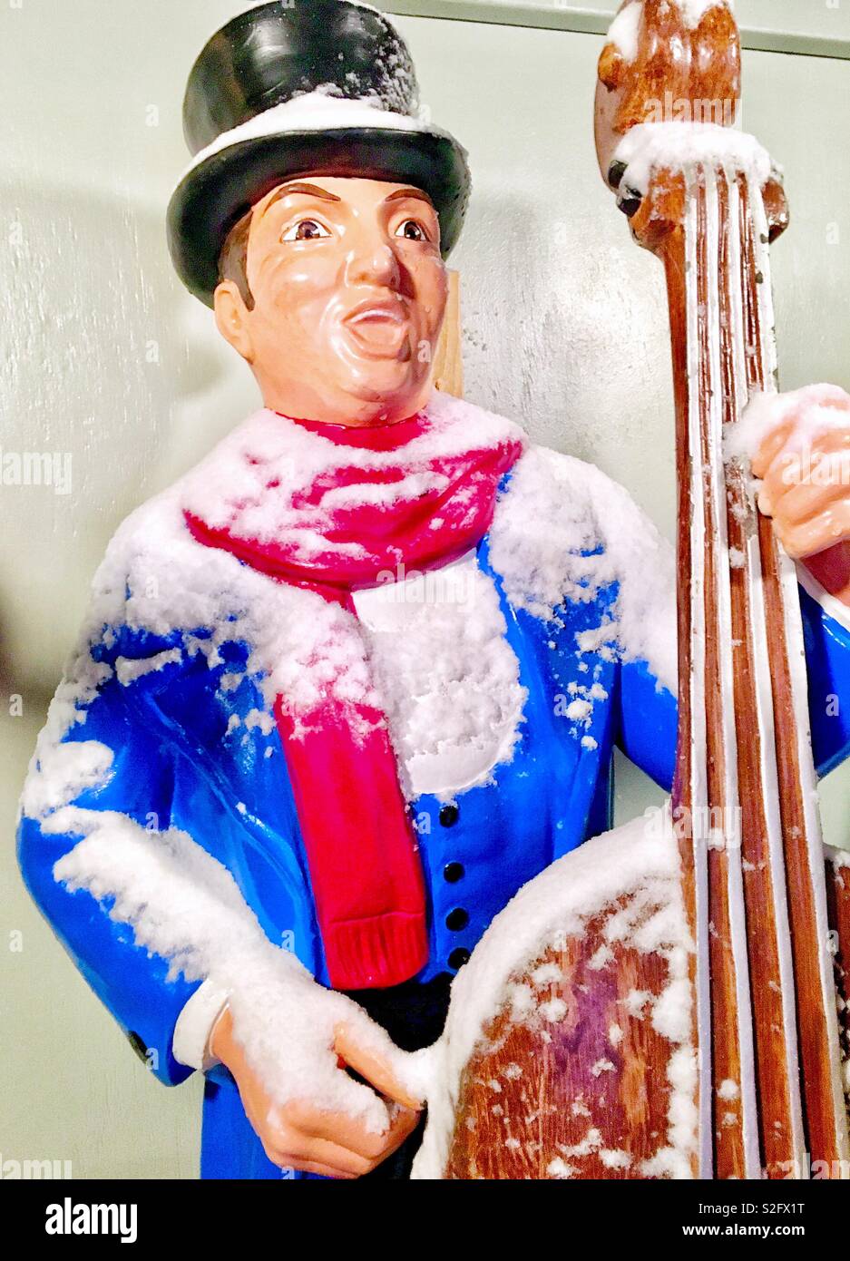 Christmas lawn ornament Singing Caroler with cello red scarf blue coat and bowler hat covered in fresh snow - Smartphone Captured Stock Image