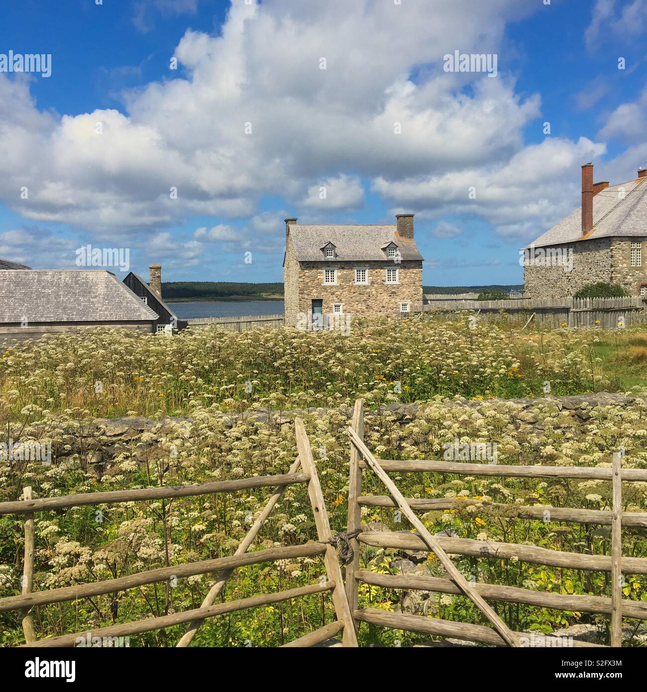Barns at Louisbourg fortress with an old wooden gate and a field with wildflowers - Smartphone Captured Stock Image