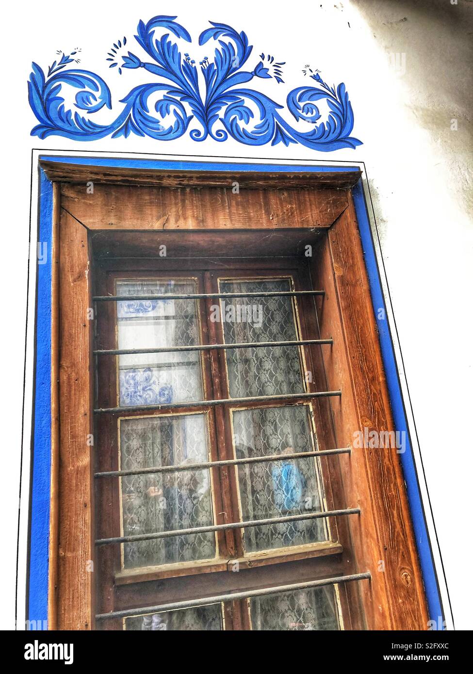 A blue floral design painted around a wooden framed window. - Smartphone Captured Stock Image