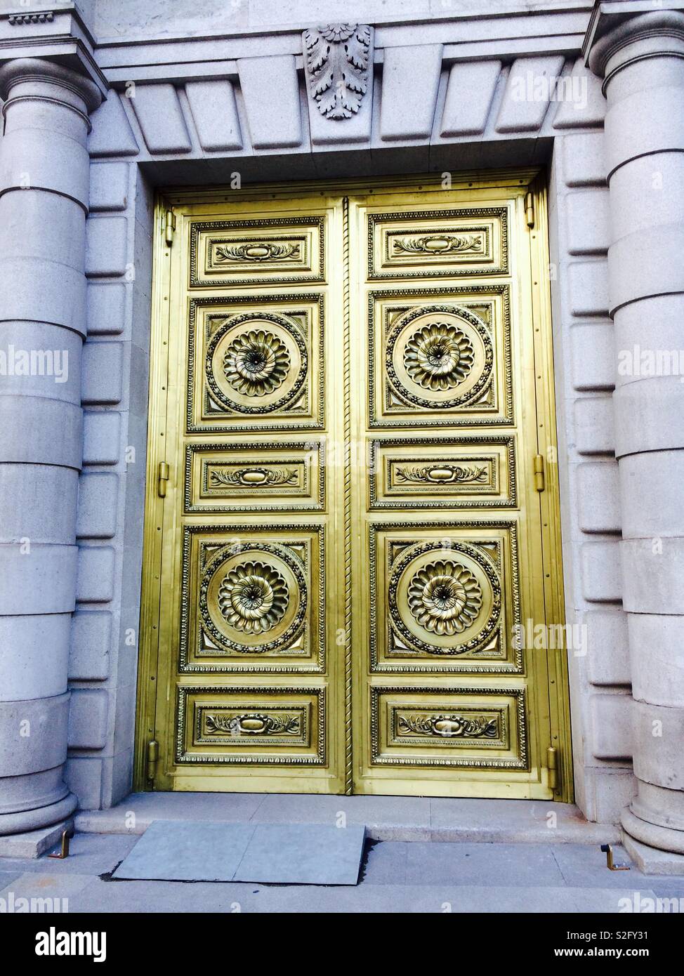 Gold or Golden double doors with intricate details carved into the design and very decorative on a building in Madrid, Spain - Smartphone Captured Stock Image