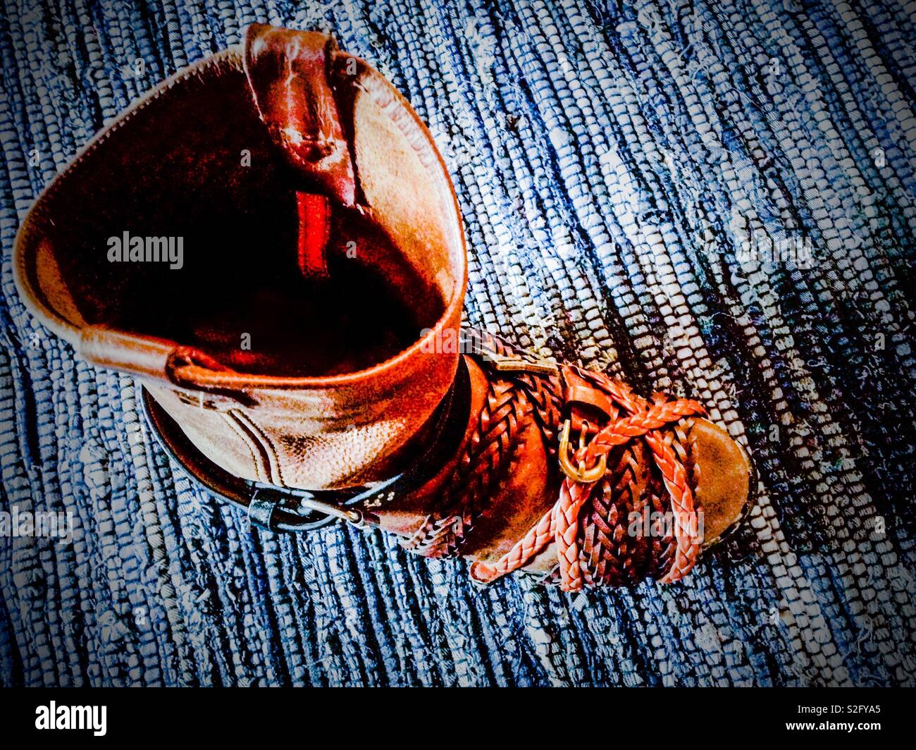Cowboy boot on blue braided rug wrapped in leather belts to clamp while glue repair dries - Smartphone Captured Stock Image