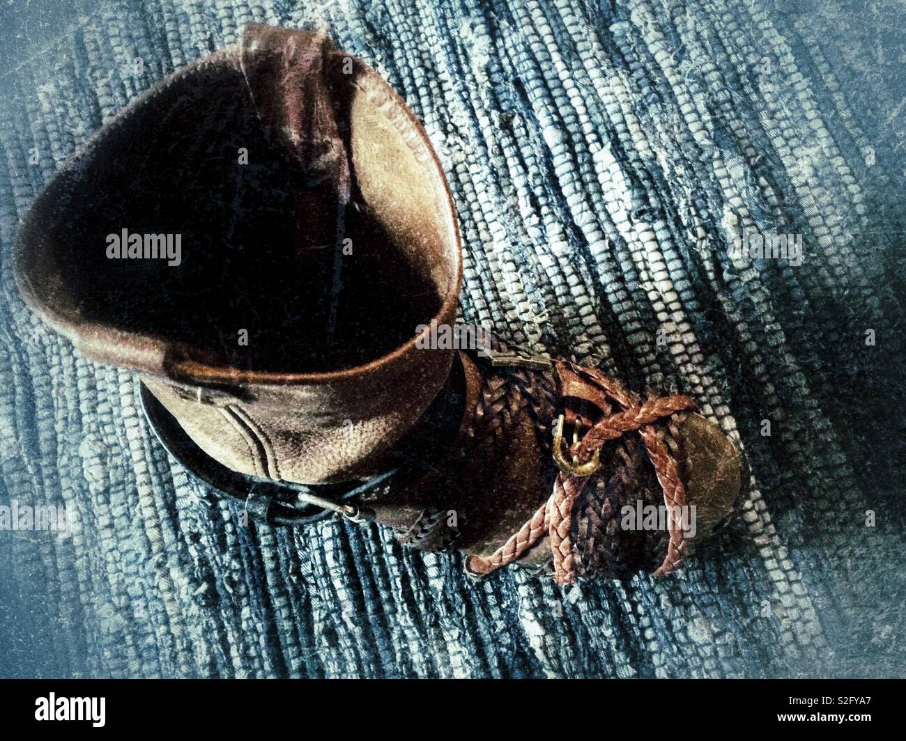 Beloved broken-in cowboy boot being repaired with glue and leather belt clamps- on blue braided rug Stock Photo