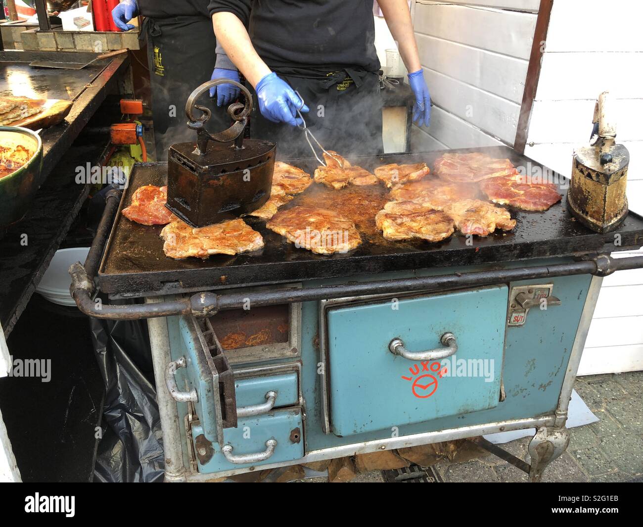 Budapest, Hungary - November 9, 2018: Christmas Market and Winter Festival at Vörösmarty Square - Pork being pressed and cooked over a coal fired Luxor grill - Image Stock Photo