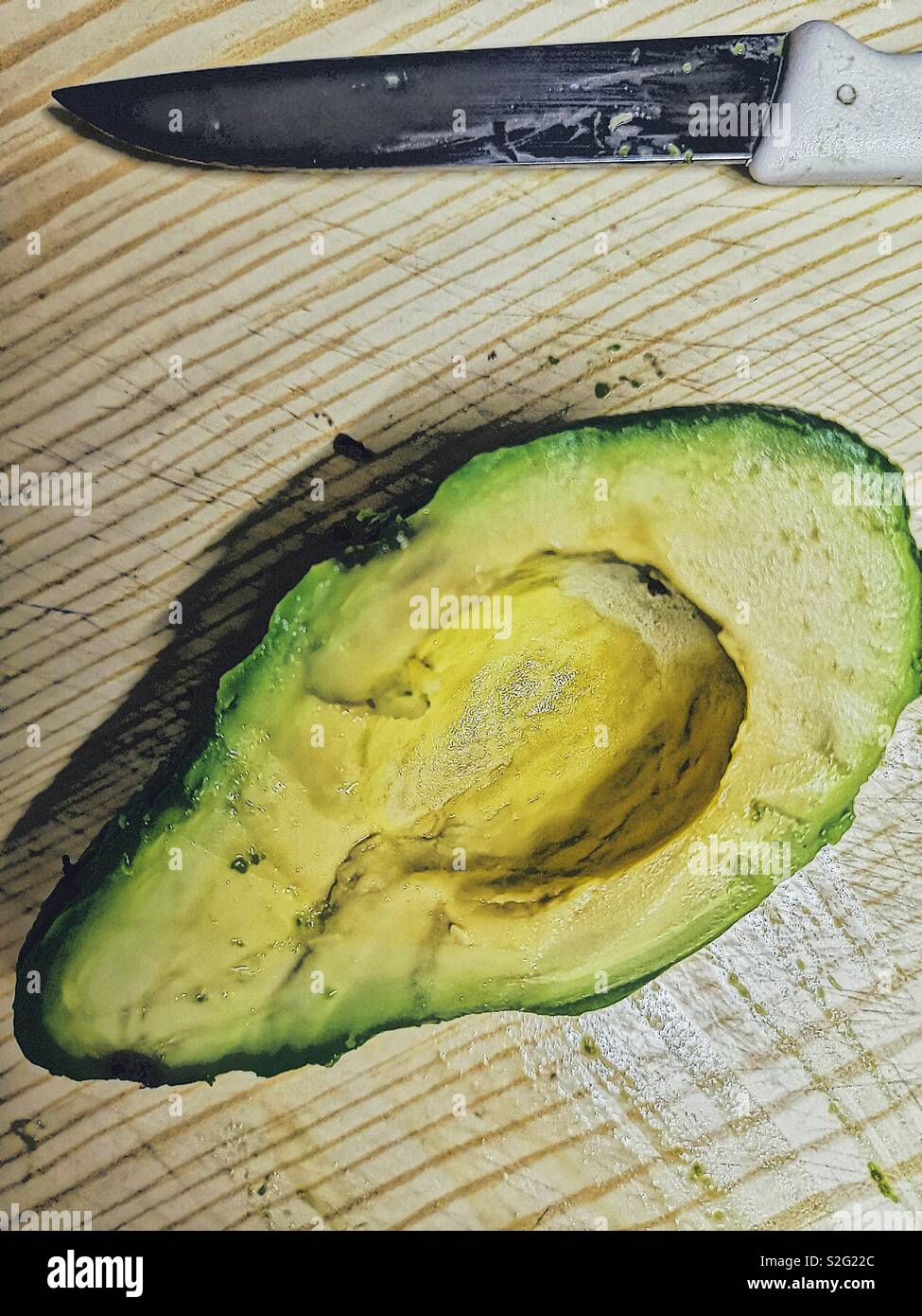 High angle shot of half an avocado on chopping board with knife Stock Photo