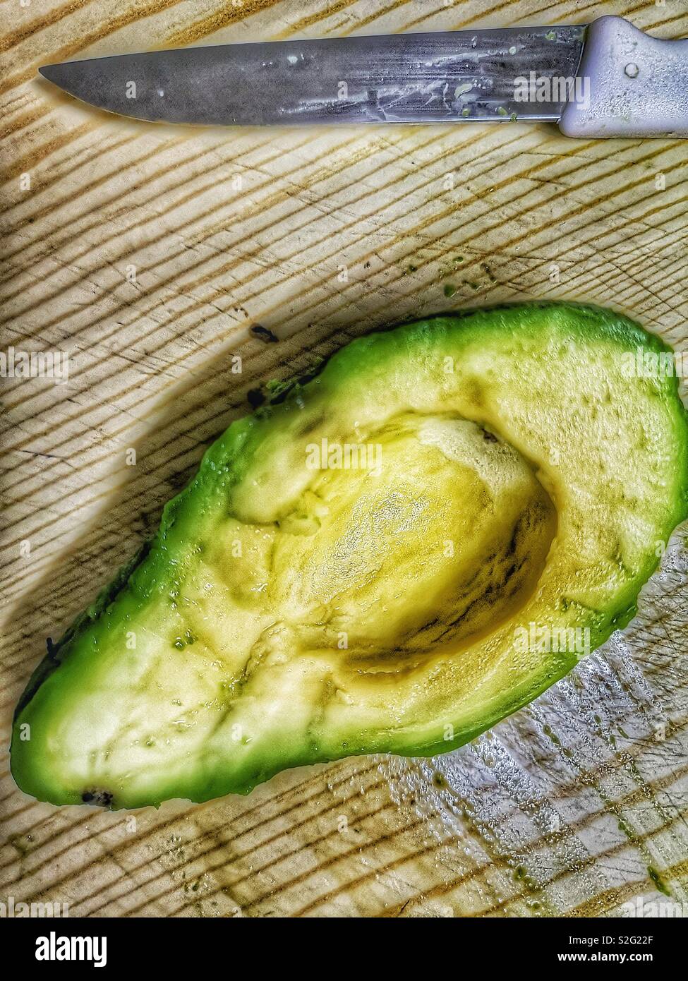 Half avocado with knife on chopping board view from above Stock Photo