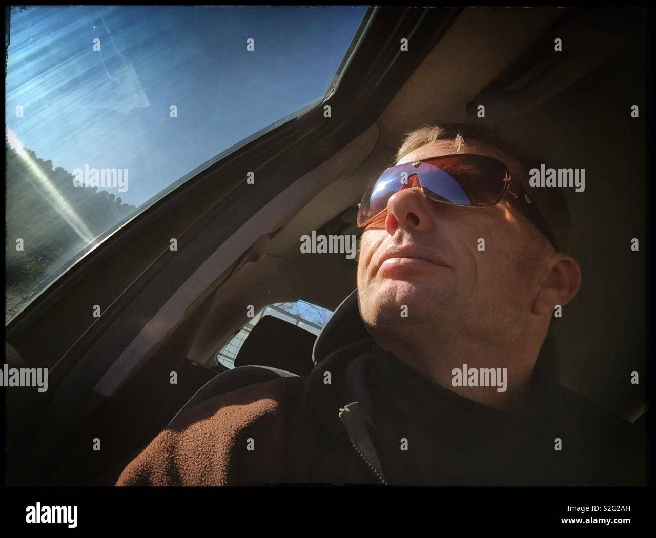 Man in the driving seat of a car with Sun on the window and a clear sky, Spain. - Smartphone Captured Stock Image