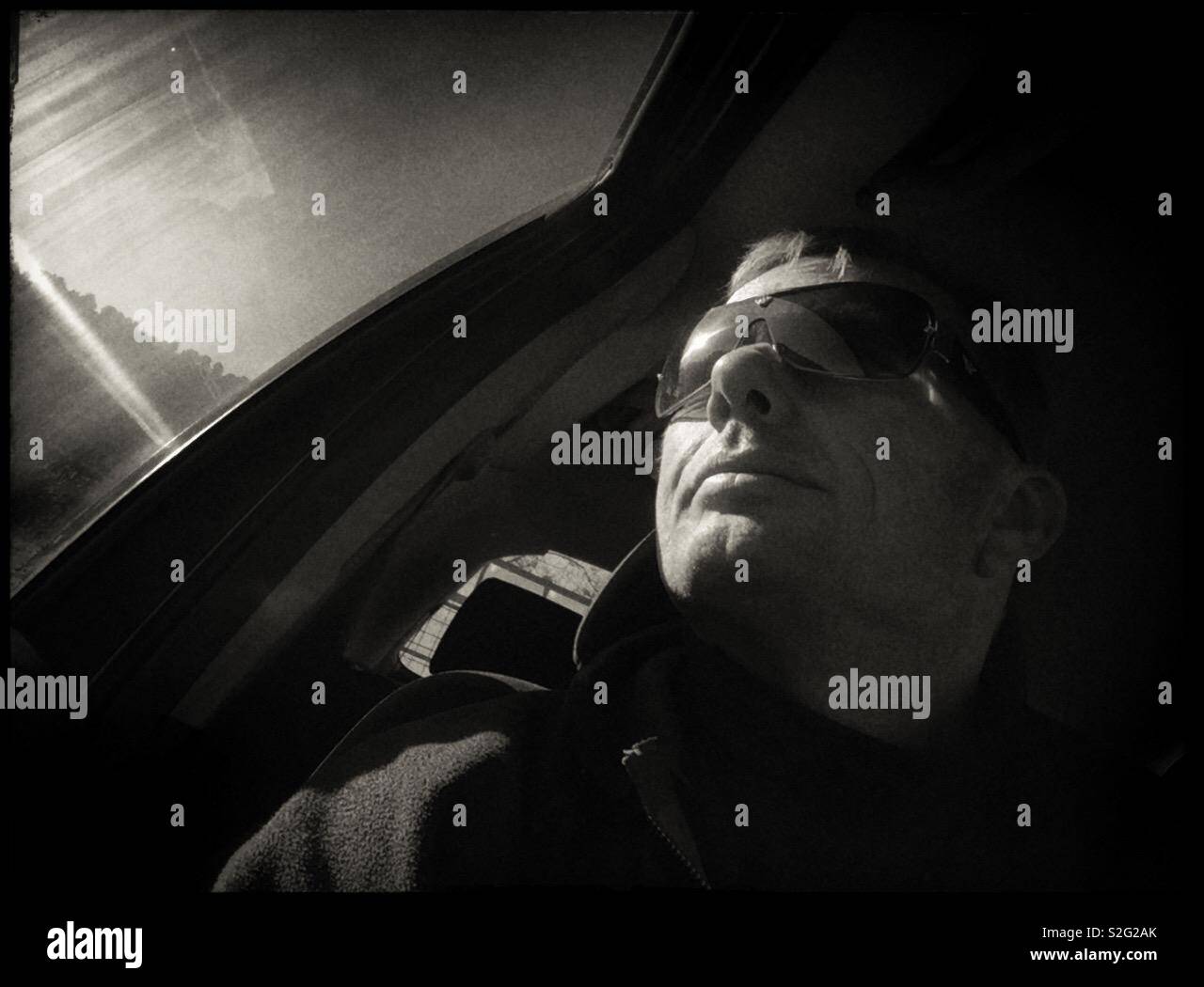 Man in the driving seat of a car with Sun on the window and a clear sky, Spain. - Smartphone Captured Stock Image
