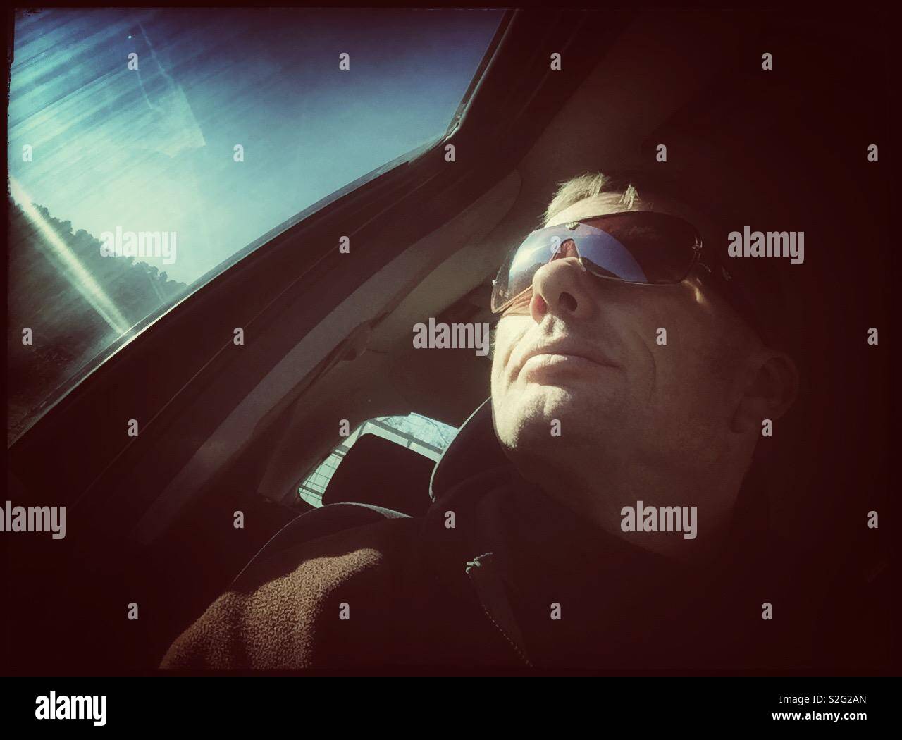 Man in the driving seat of a car with Sun on the window and a clear sky, Spain. - Smartphone Captured Stock Image