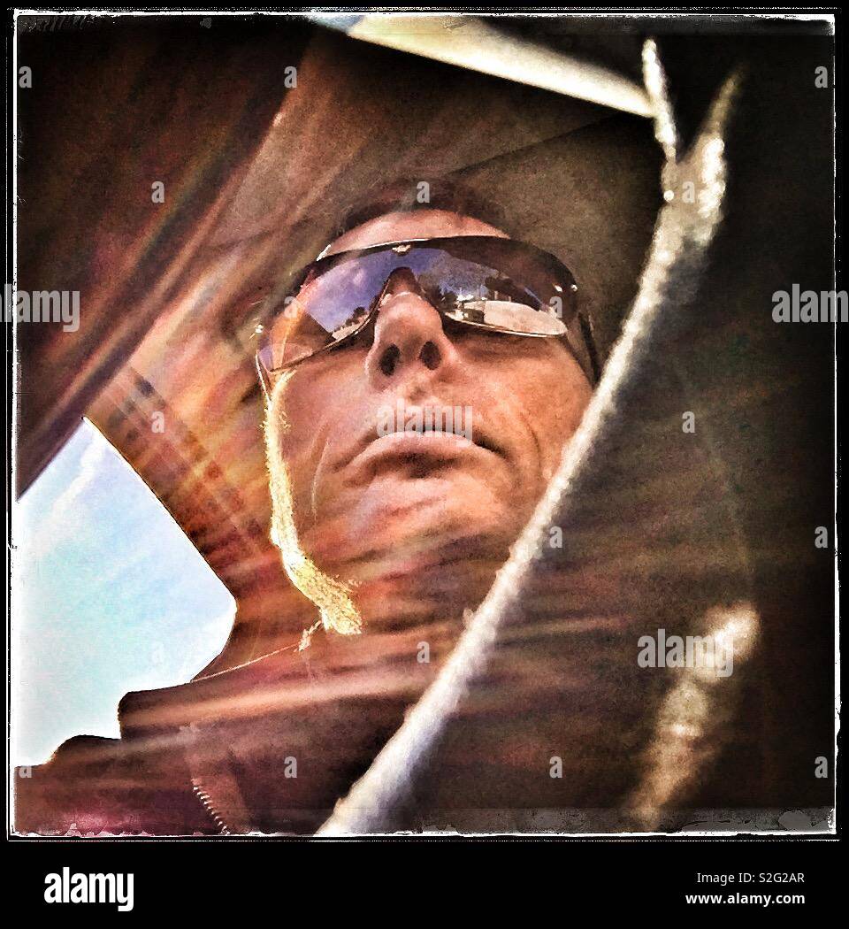 Man in the driving seat of a car with Sun on the window and a clear sky, Spain. - Smartphone Captured Stock Image