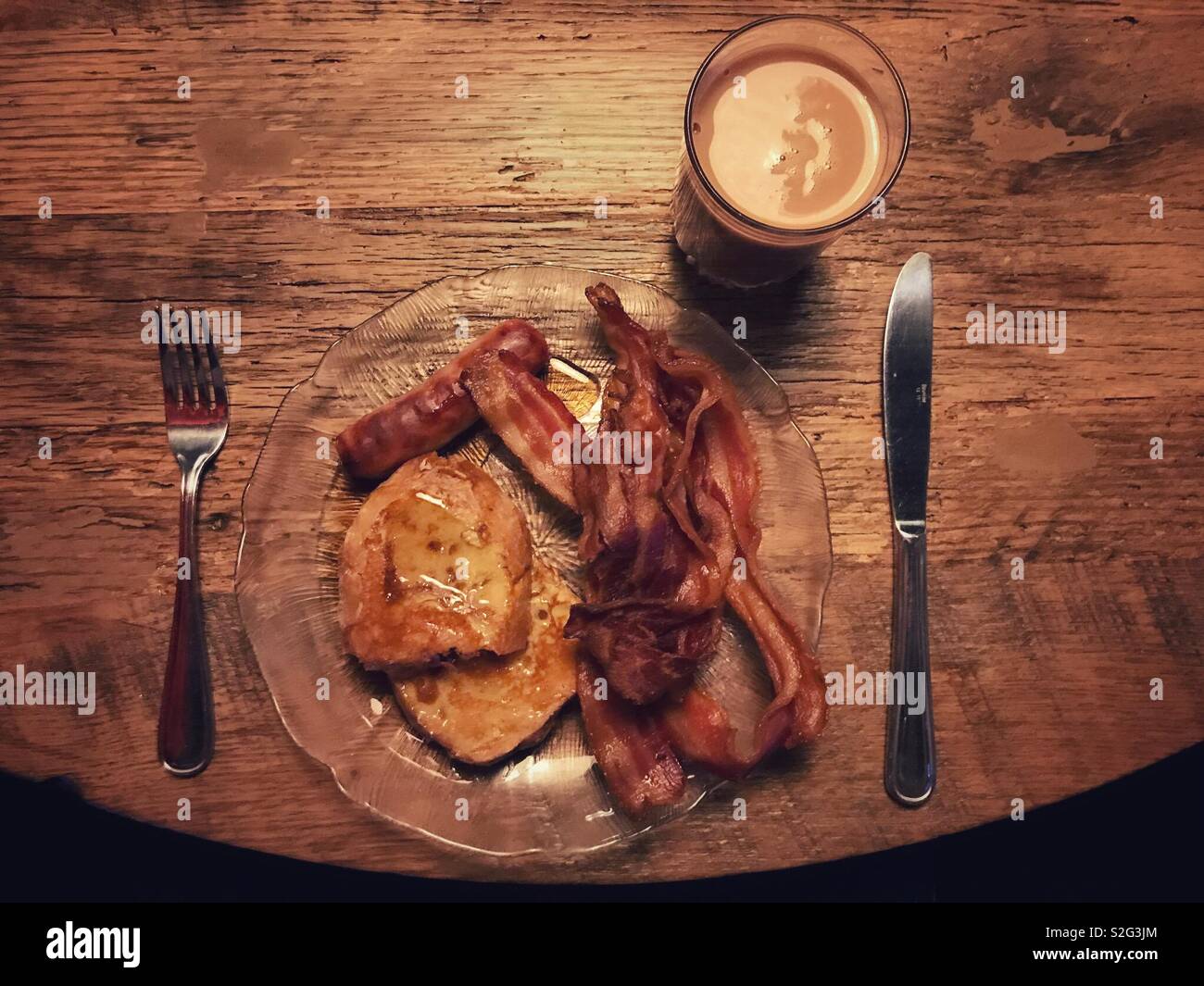 A very brown meal of chocolate milk, bacon, sausage, and french toast with maple syrup, on a wooden table top. - Smartphone Captured Stock Image