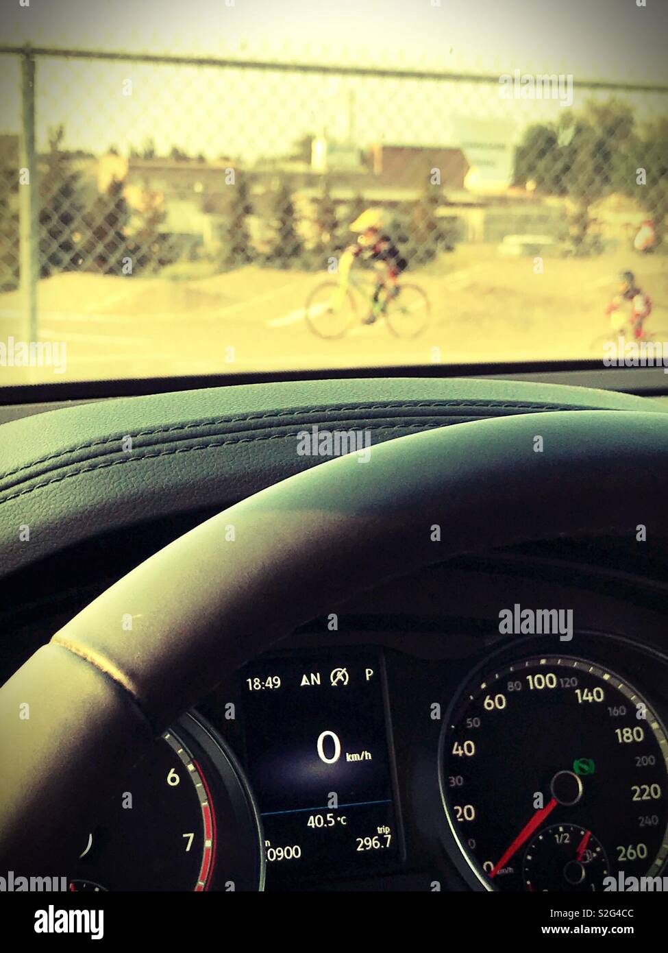 Kids race in full protective gear on a BMX track, viewed from a vehicle with the temperature gauge showing the outside temperature at 40.5 degrees Celsius. Stock Photo