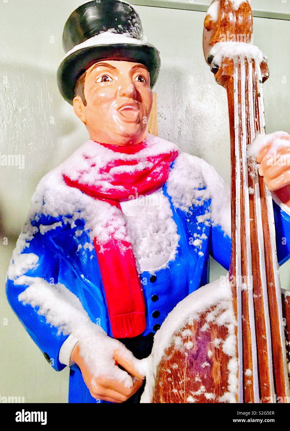 Christmas lawn ornament Singing Caroler with cello red scarf blue coat and bowler hat covered in fresh snow - Smartphone Captured Stock Image