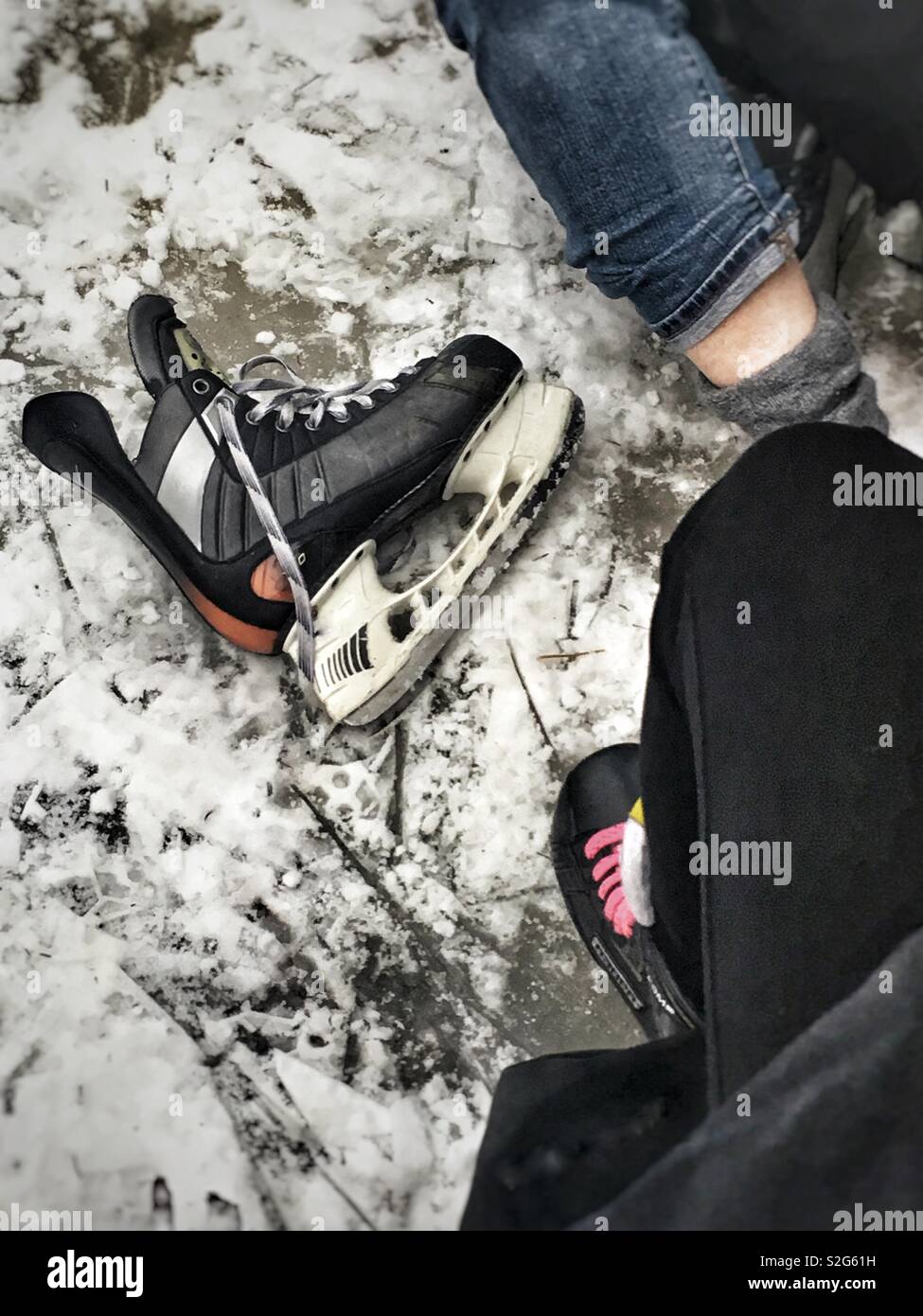 Just a skate, a single hockey skate sits on the ice beside person putting the other one on. Winter lake ice skating, light snow covering Stock Photo