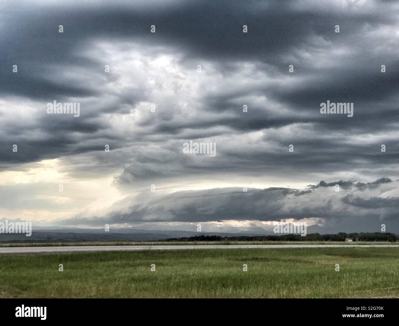 A shelf cloud hangs low over a foothills landscape with ominous clouds above. Stock Photo