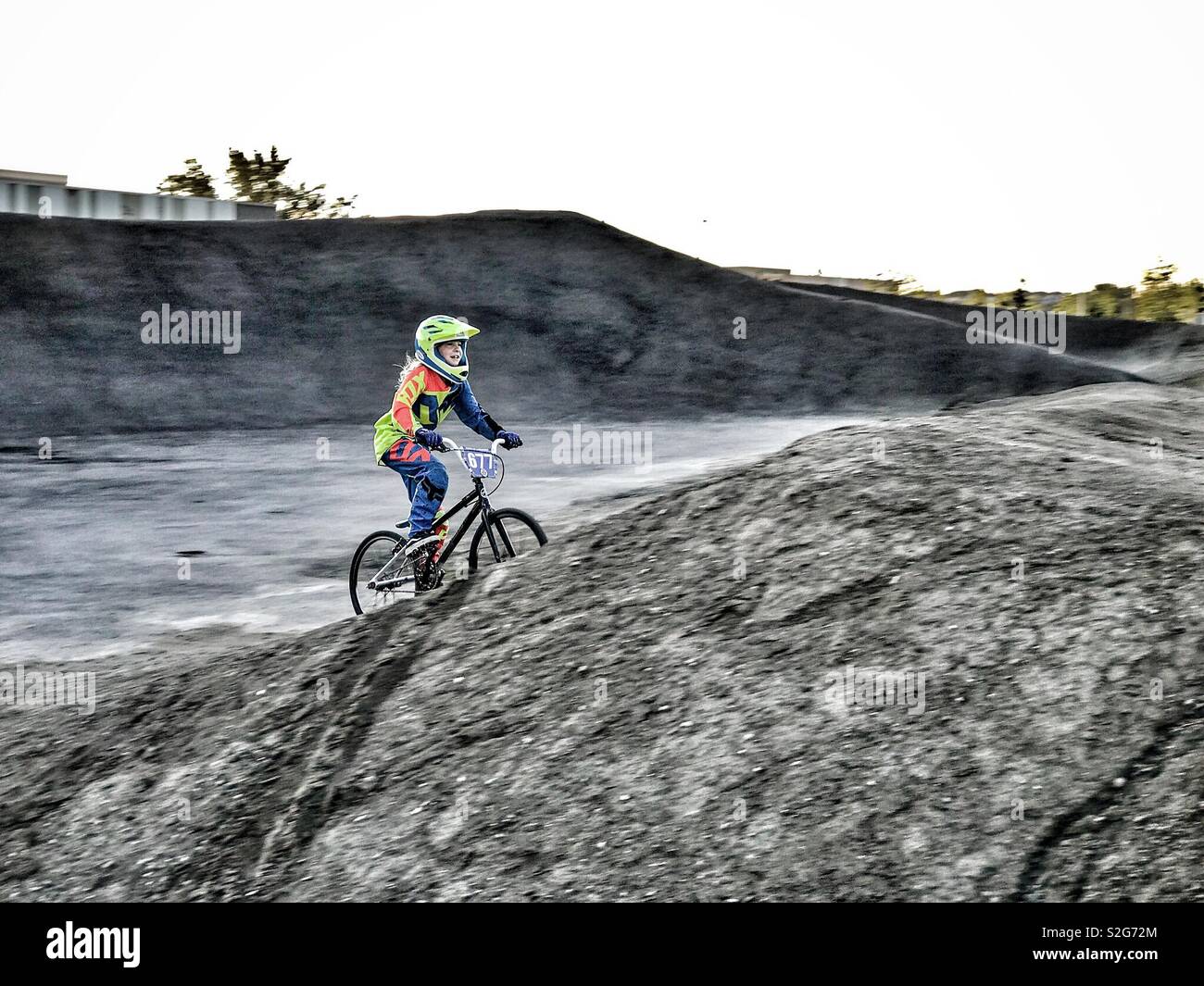 A girl races her BMX bike at a gritty dirt and asphalt track. Stock Photo