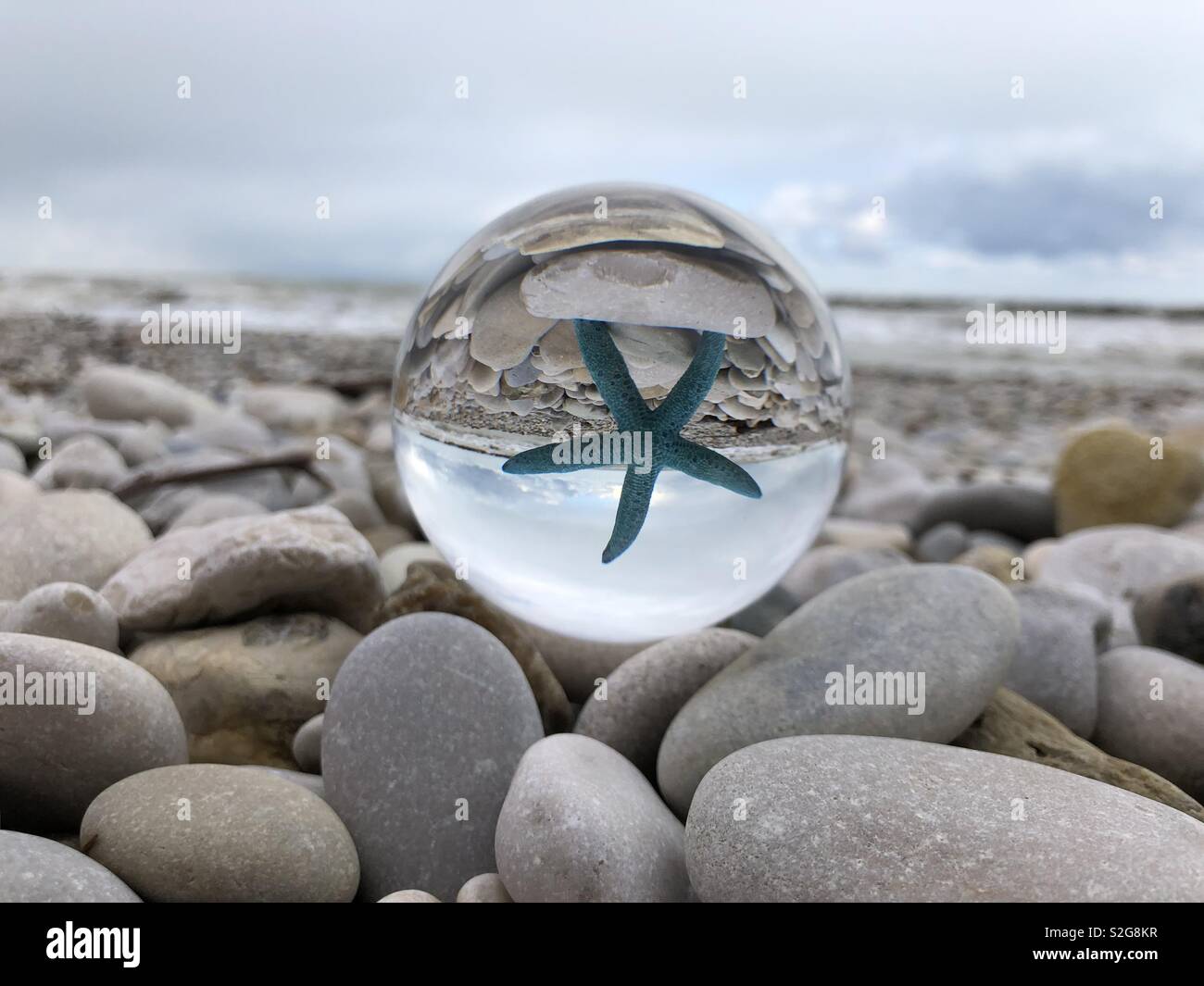 Starfish seen through a crystal ball over a pebbles beach - Smartphone Captured Stock Image