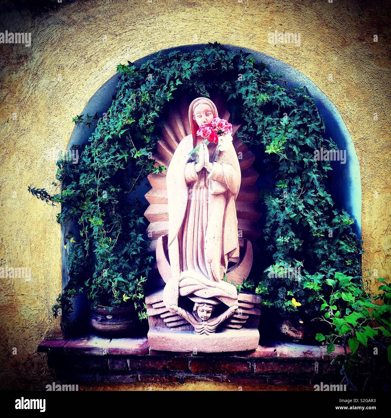A sculpture of Our Lady of Guadalupe holding roses decorates an altar in Hotel la Plaza in Tequisquiapan, Queretaro, Mexico Stock Photo
