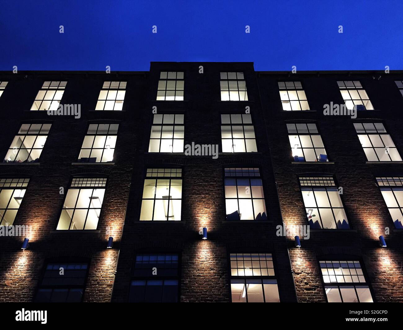 A low angle view of a modern stone building and office block at night with windows illuminated Stock Photo
