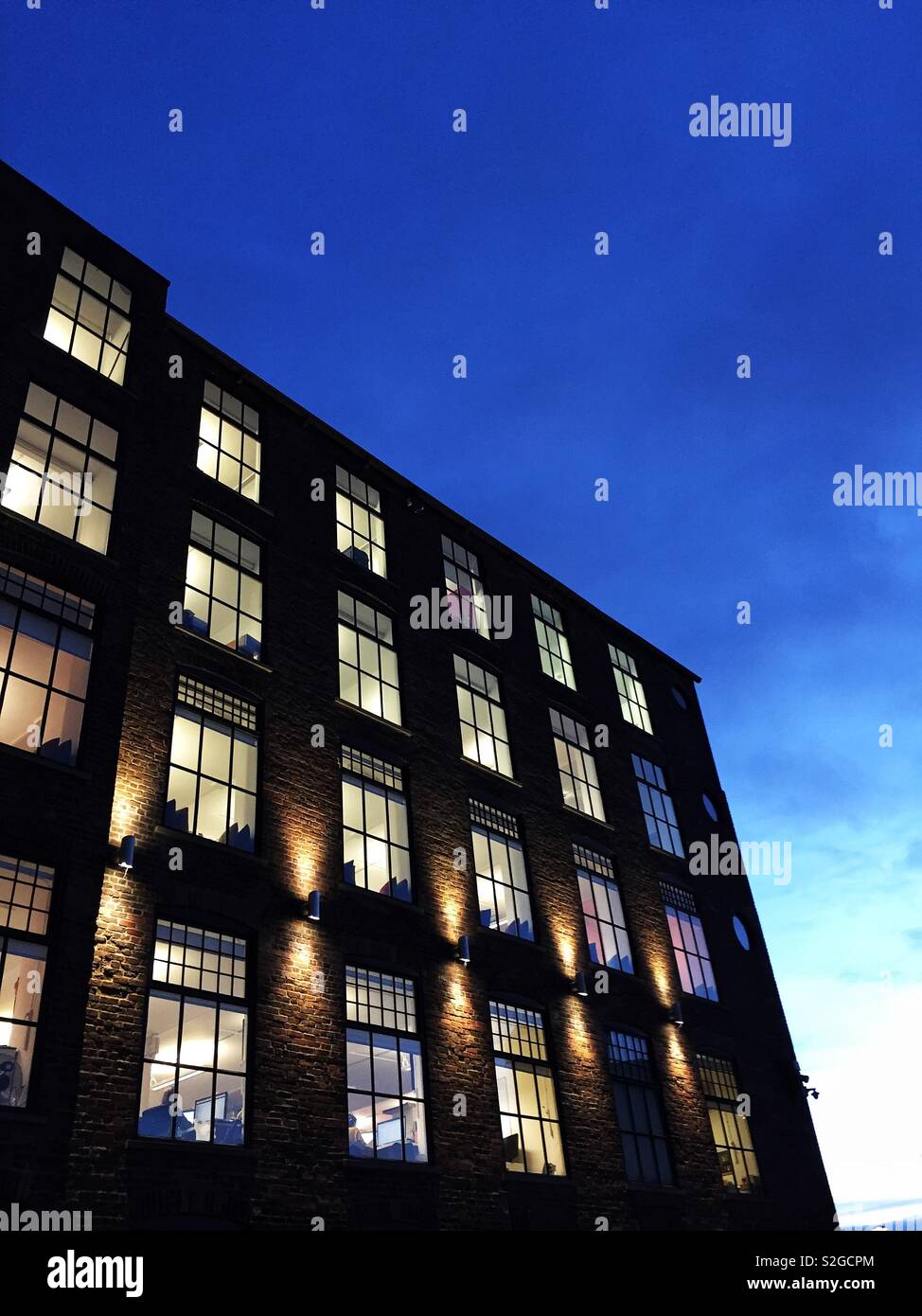 The exterior of a modern office block at night with the glow of window light in the rows of windows lighting up the interior rooms Stock Photo