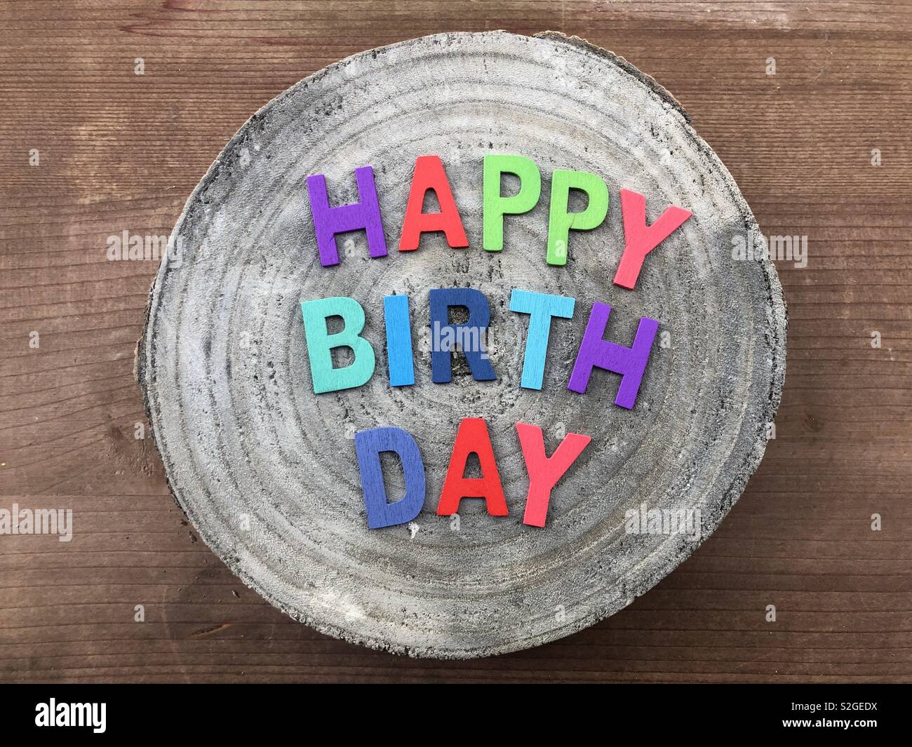 Happy Birthday text with colored wooden letters over a wooden mango round piece Stock Photo