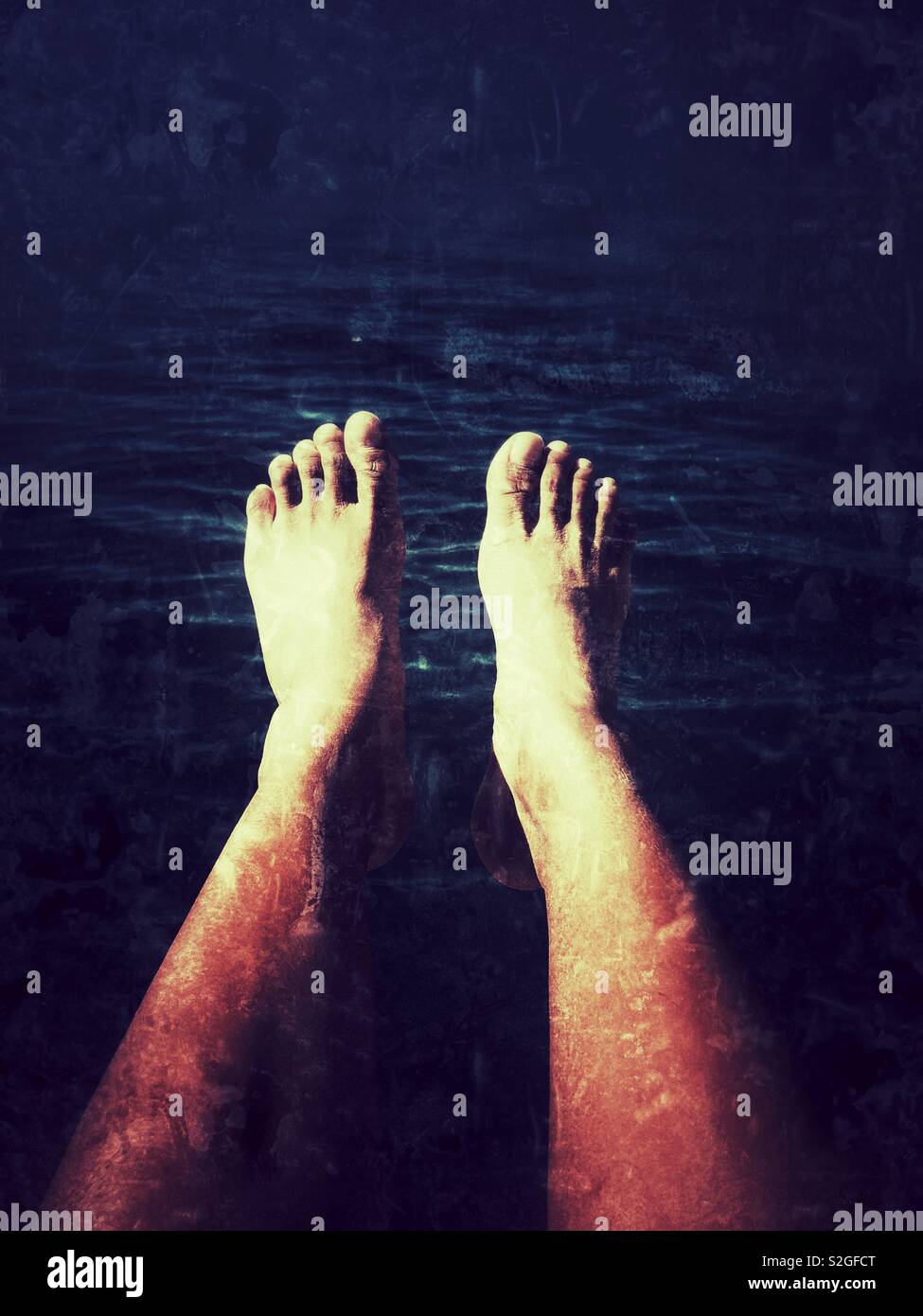 A pair of legs submerged into dark blue water Stock Photo