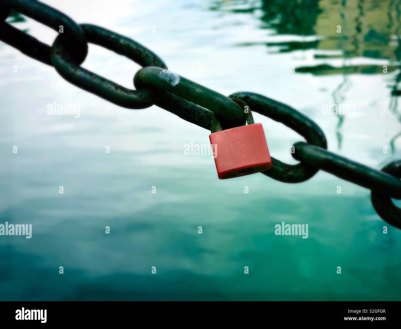 Red padlock or love lock on the rusty chain by the sea - Smartphone Captured Stock Image