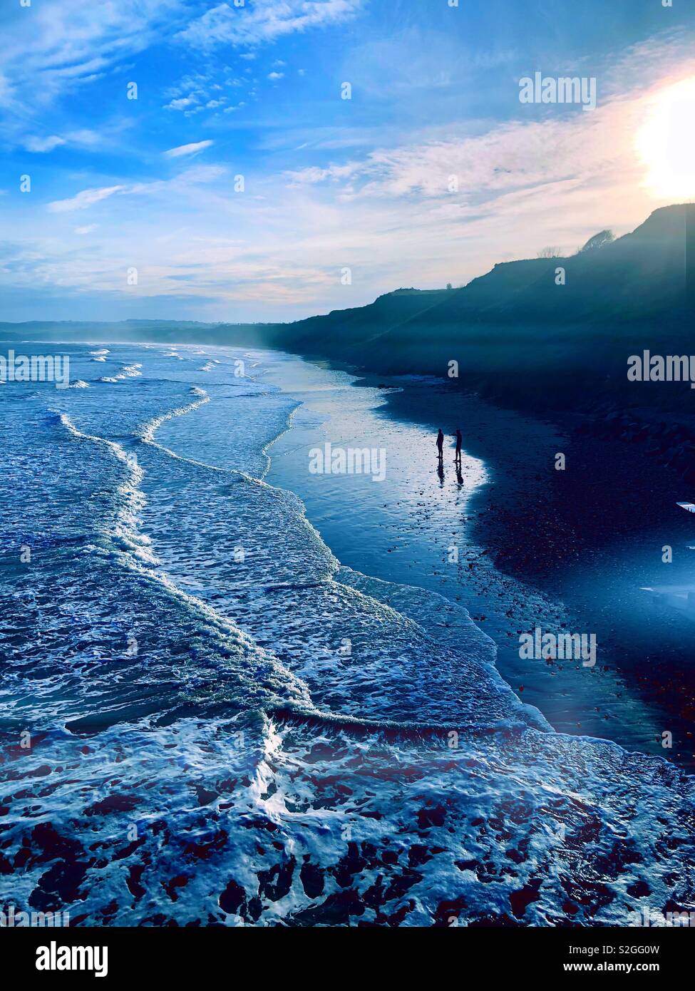 2 figures on a beach at high tide in winter with low sun Stock Photo