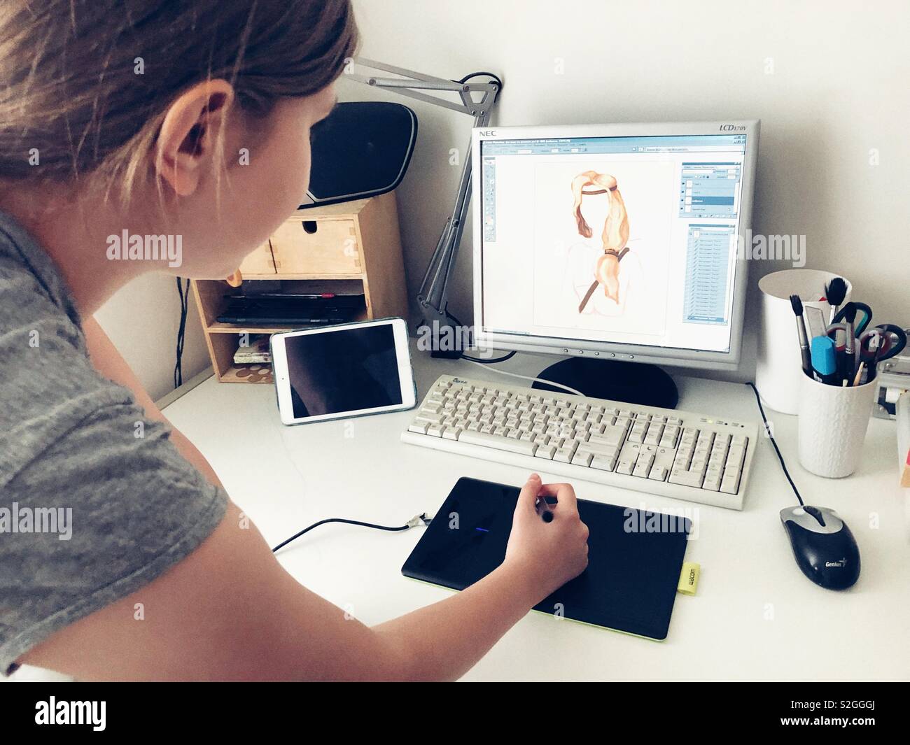 Teen girl sketching with stylus on graphic tablet at the desk with computer - Smartphone Captured Stock Image
