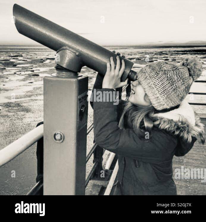 Young girl looking through a telescope at the seaside on a winter’s day