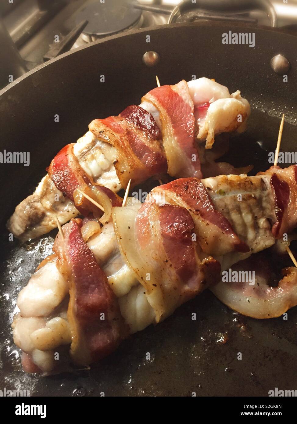 Monkfish fillet wrapped in bacon sautéing in a skillet, USA - Smartphone Captured Stock Image