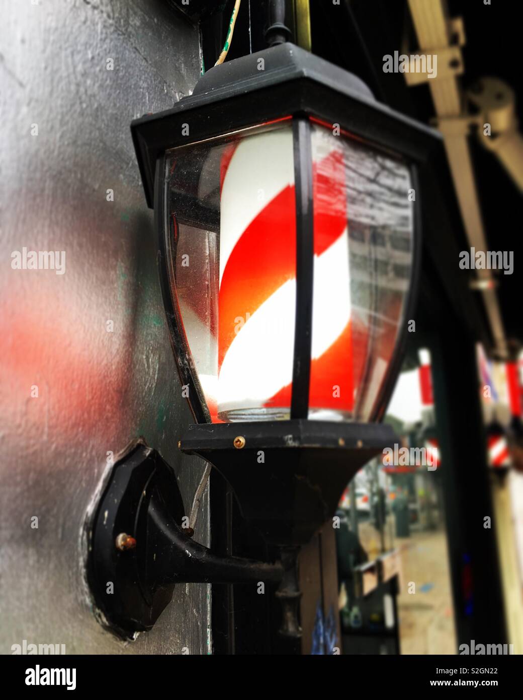 Modern electric version of the traditional barbers shop sign, outside a barber / hairdresser, illuminated and turning during opening hours. England, UK - Smartphone Captured Stock Image