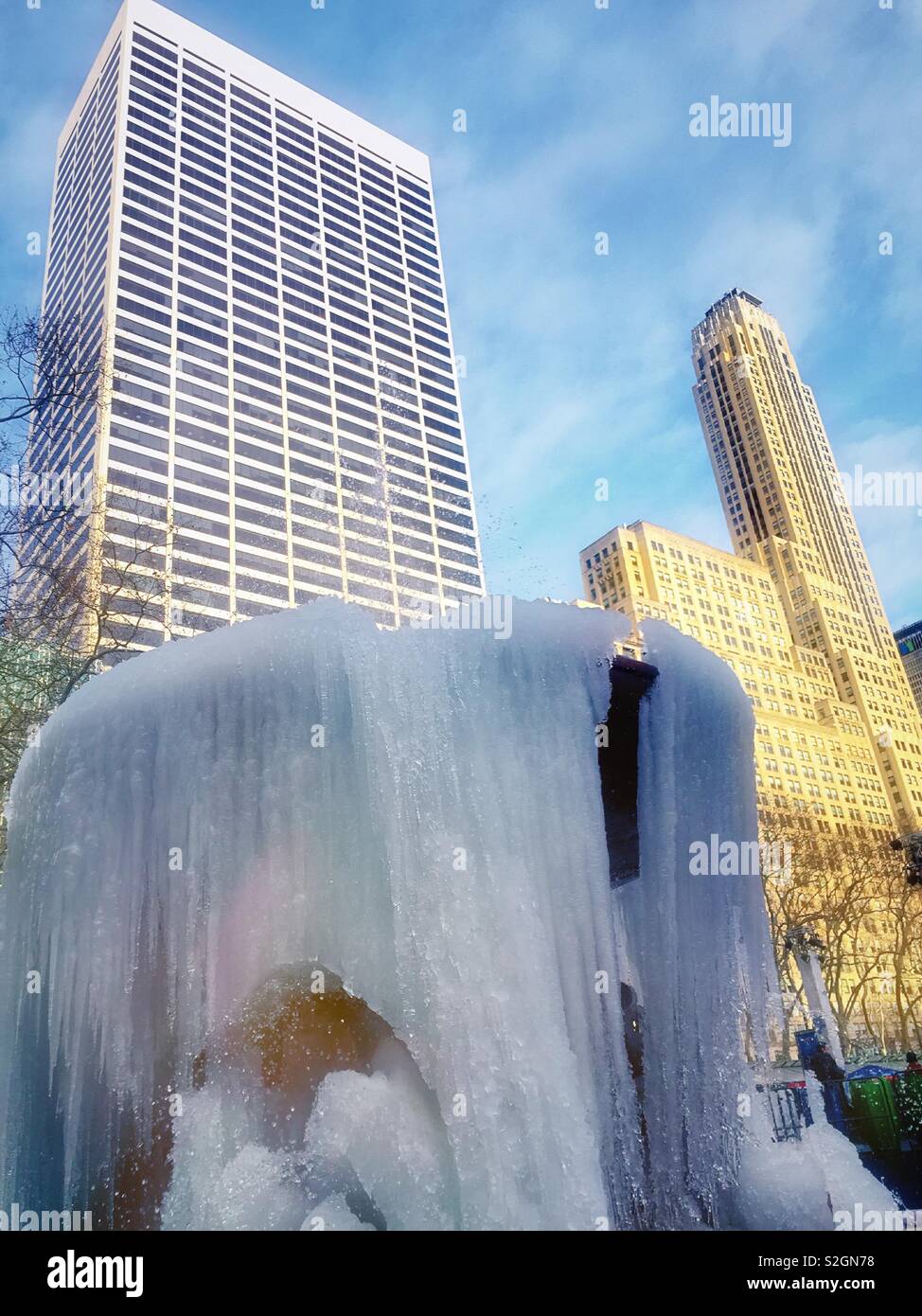 Icicles hanging from the Josephine Shaw Lowell memorial fountain in Bryant Park with midtown Manhattan skyscrapers in the background, NYC, USA - Smartphone Captured Stock Image