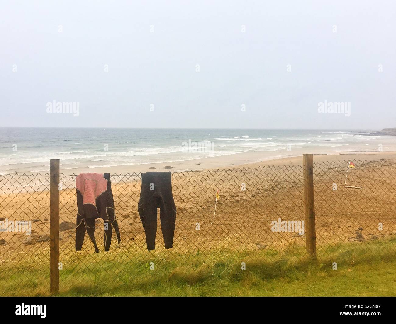 Wetsuits tossed over a wire fence in bad weather at the beach in Ireland. September 2018 - Smartphone Captured Stock Image