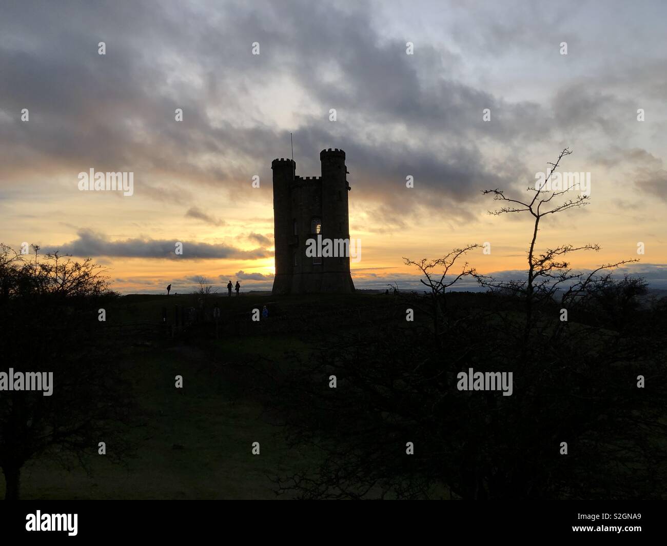 Broadway Hill Tower, Cotswolds, silhouetted against a dramatic sunset back ground with walkers in profile on the ridge line. - Smartphone Captured Stock Image