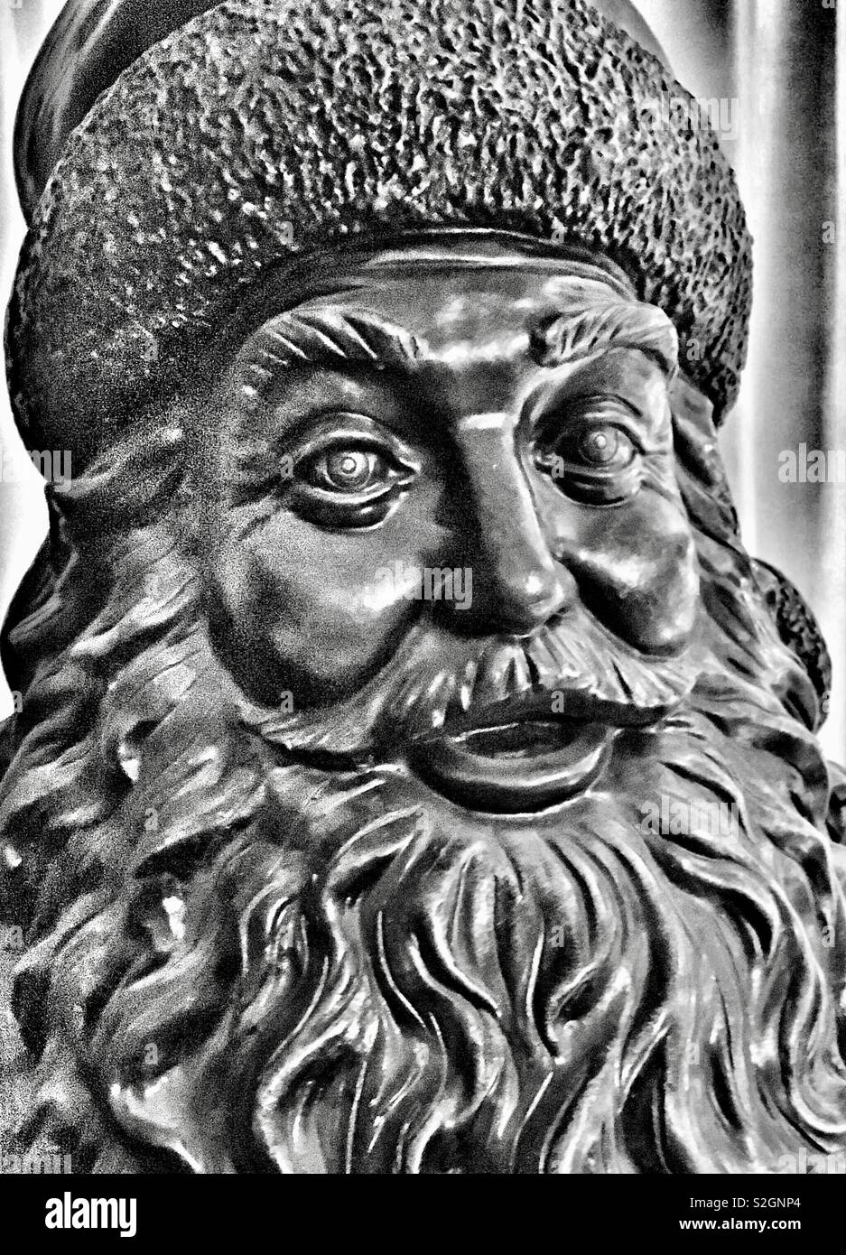 Closeup of bronze creepy Santa statue with wide eyes and fur hat in black and white Stock Photo