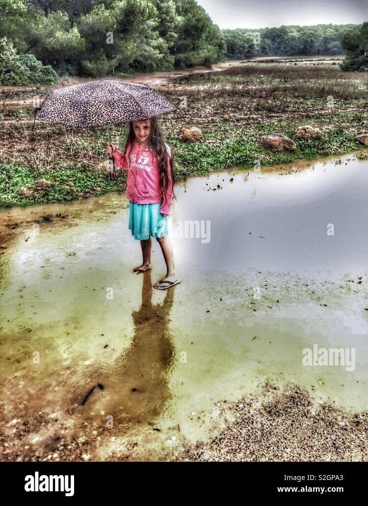 Little girl in the rain holding an umbrella and standing in a puddle