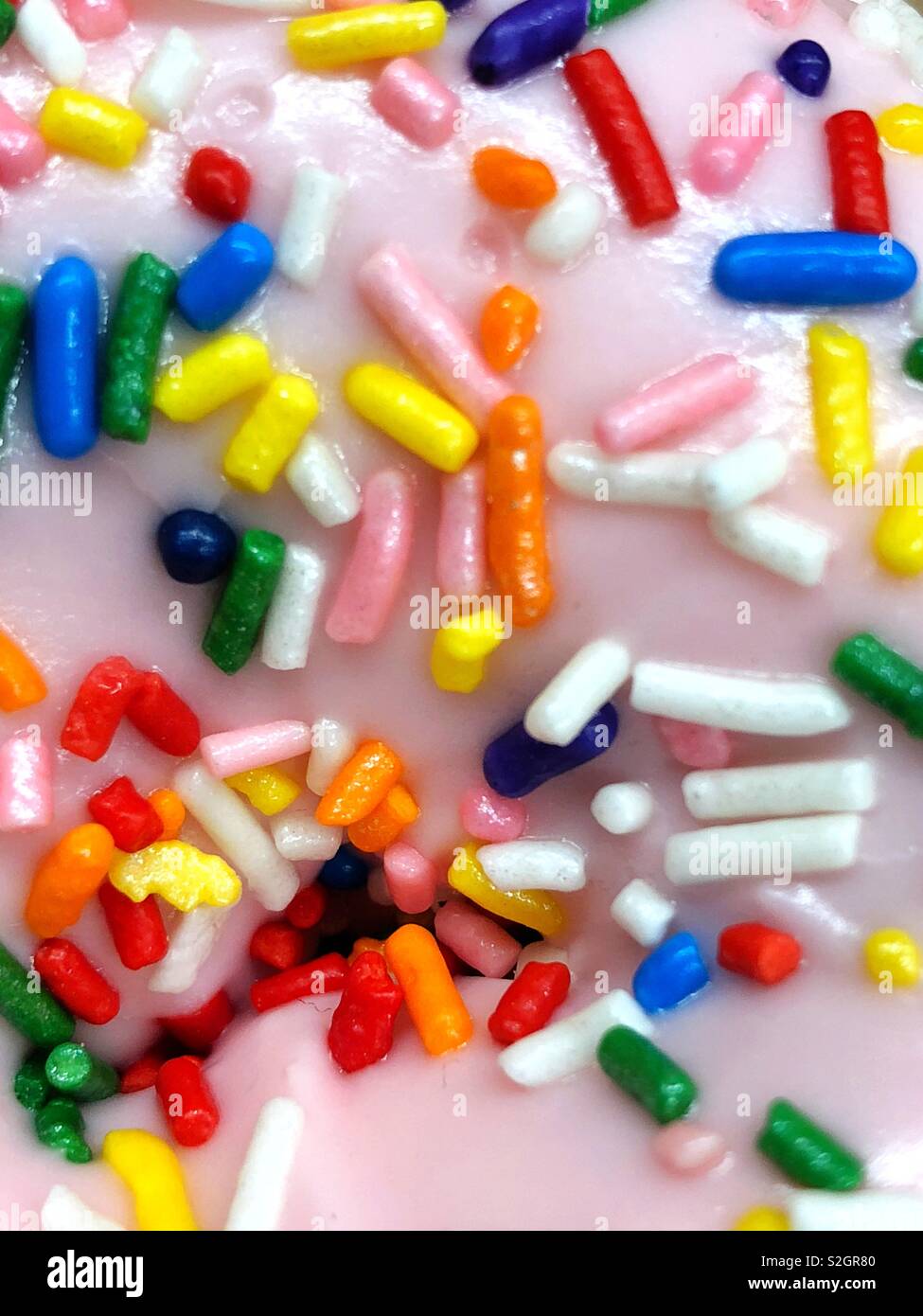 colorful rainbow of sprinkles on pink glazed doughnut - Smartphone Captured Stock Image