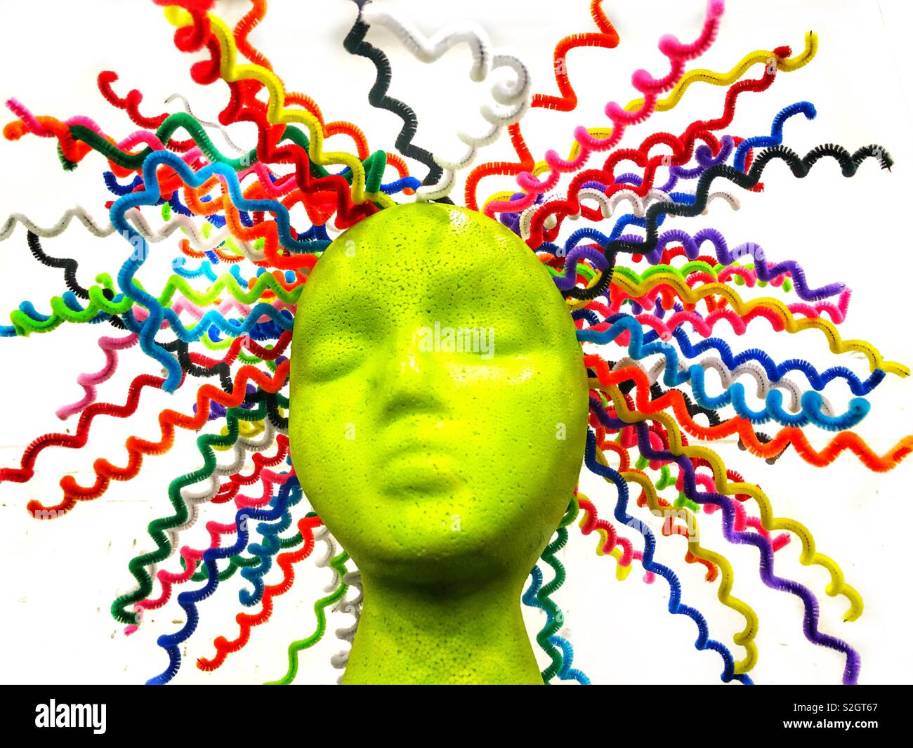 A lime green mannequin head with colorful sprains of hair protruding in all directions on a white background Stock Photo