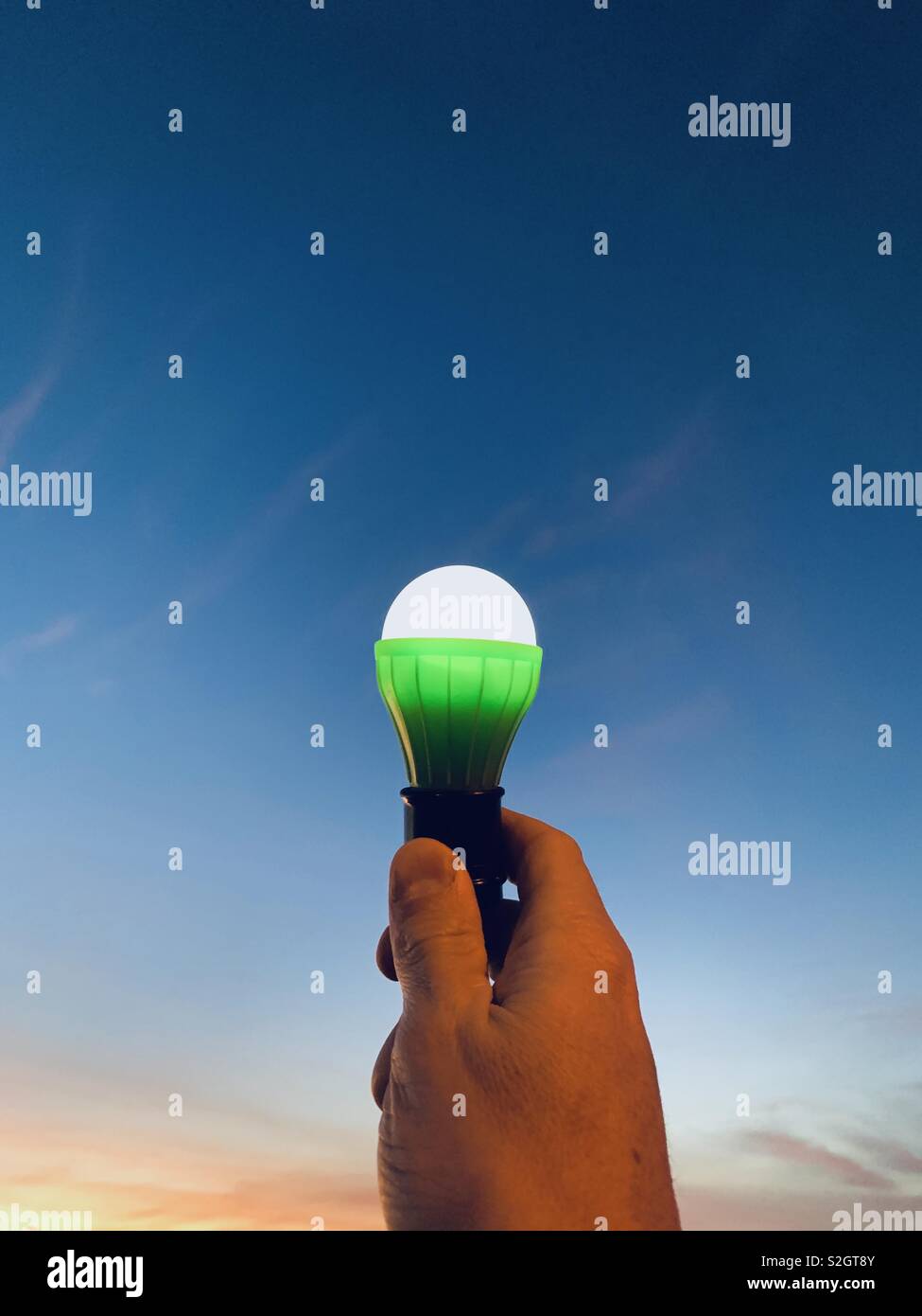 A hand holding a light bulb at sunset. Stock Photo