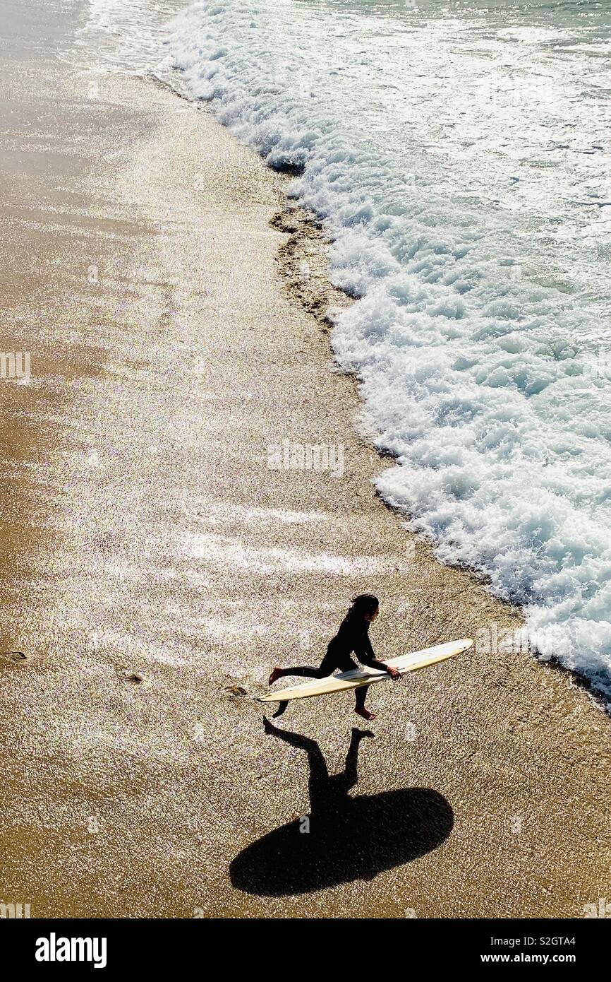 A young male surfer runs into the water. Manhattan Beach, California USA. Stock Photo