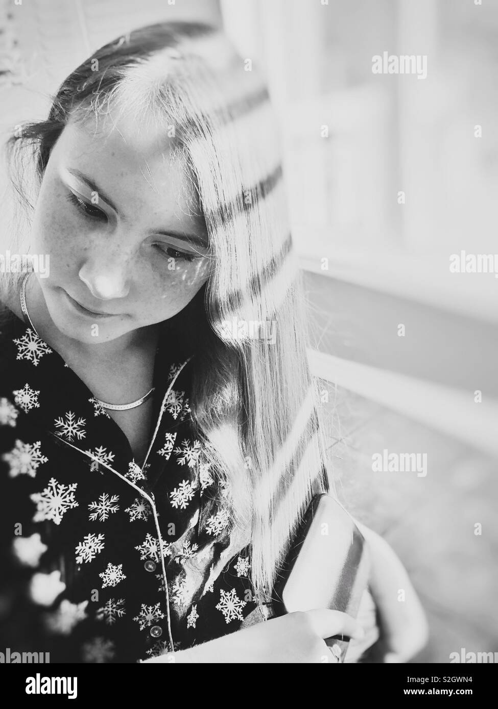 Airy black and white image of teenage girl brushing long, blonde hair by a window with sunlight and shadows Stock Photo