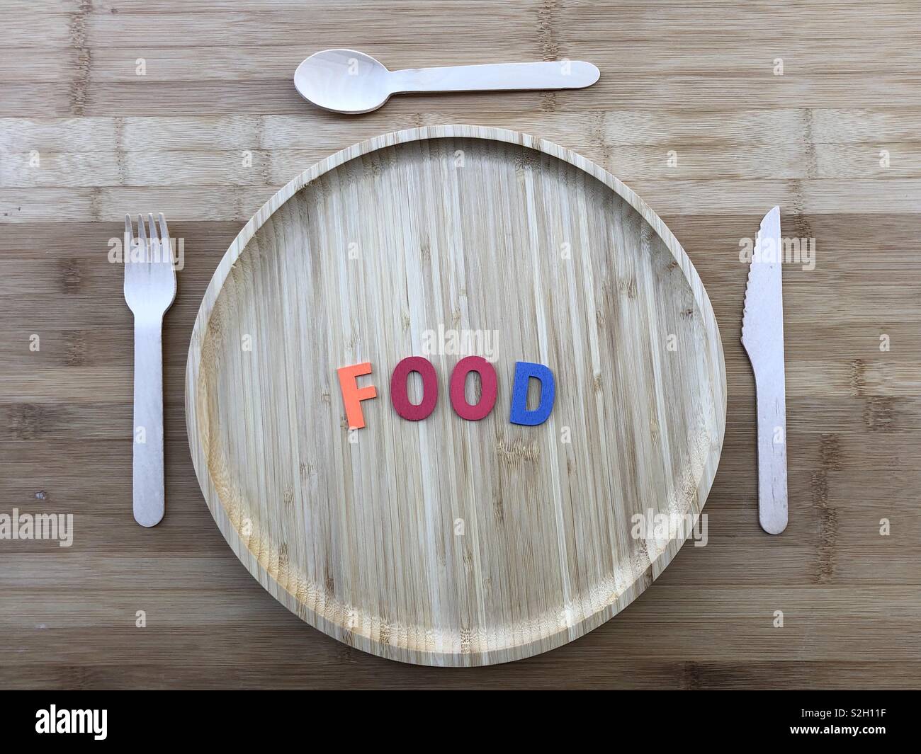 wooden dish with wooden cutlery over a wooden table abd colored wooden letters for the word Food Stock Photo