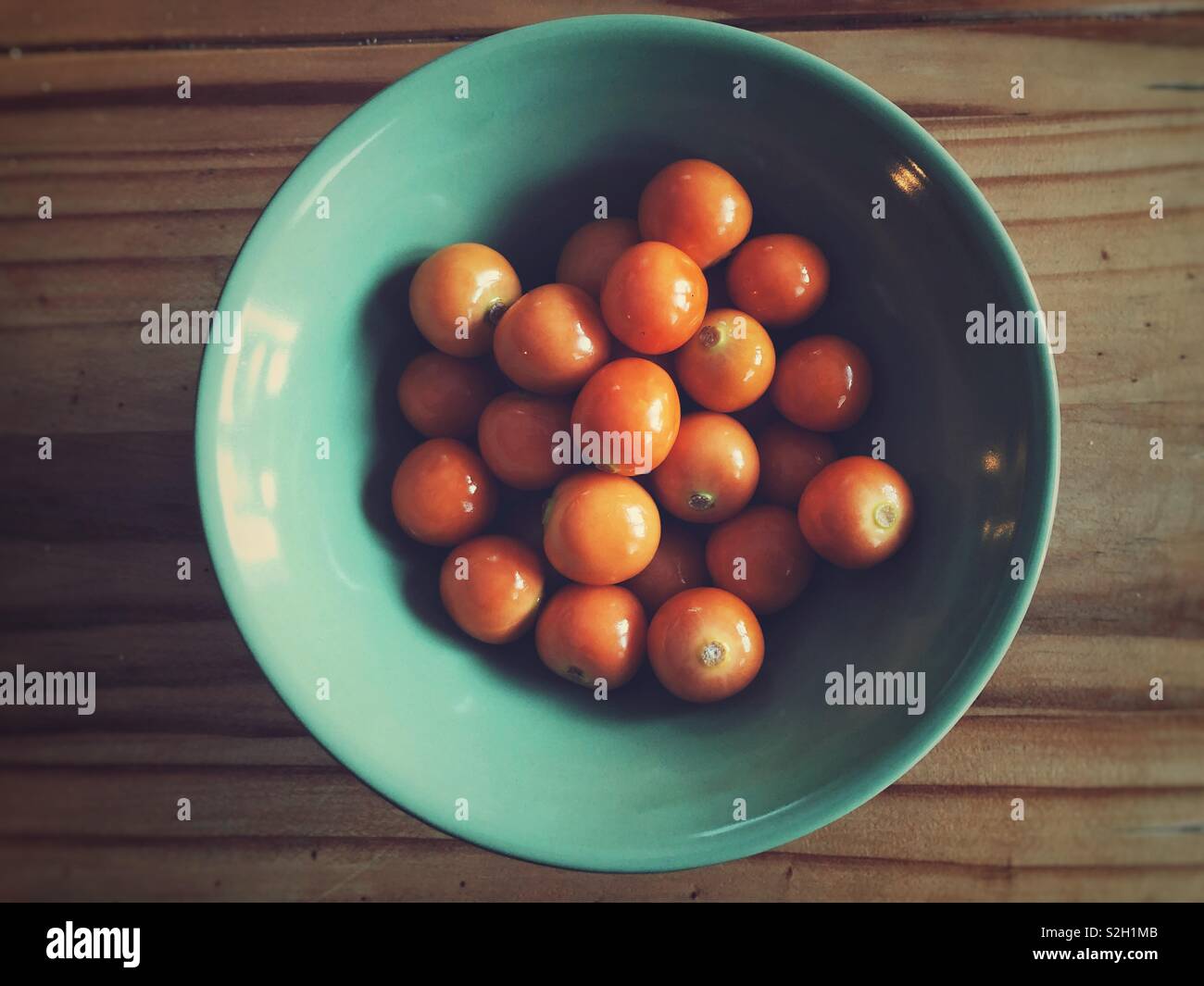 Goldenberries in a teal green bowl on a wooden table - Smartphone Captured Stock Image