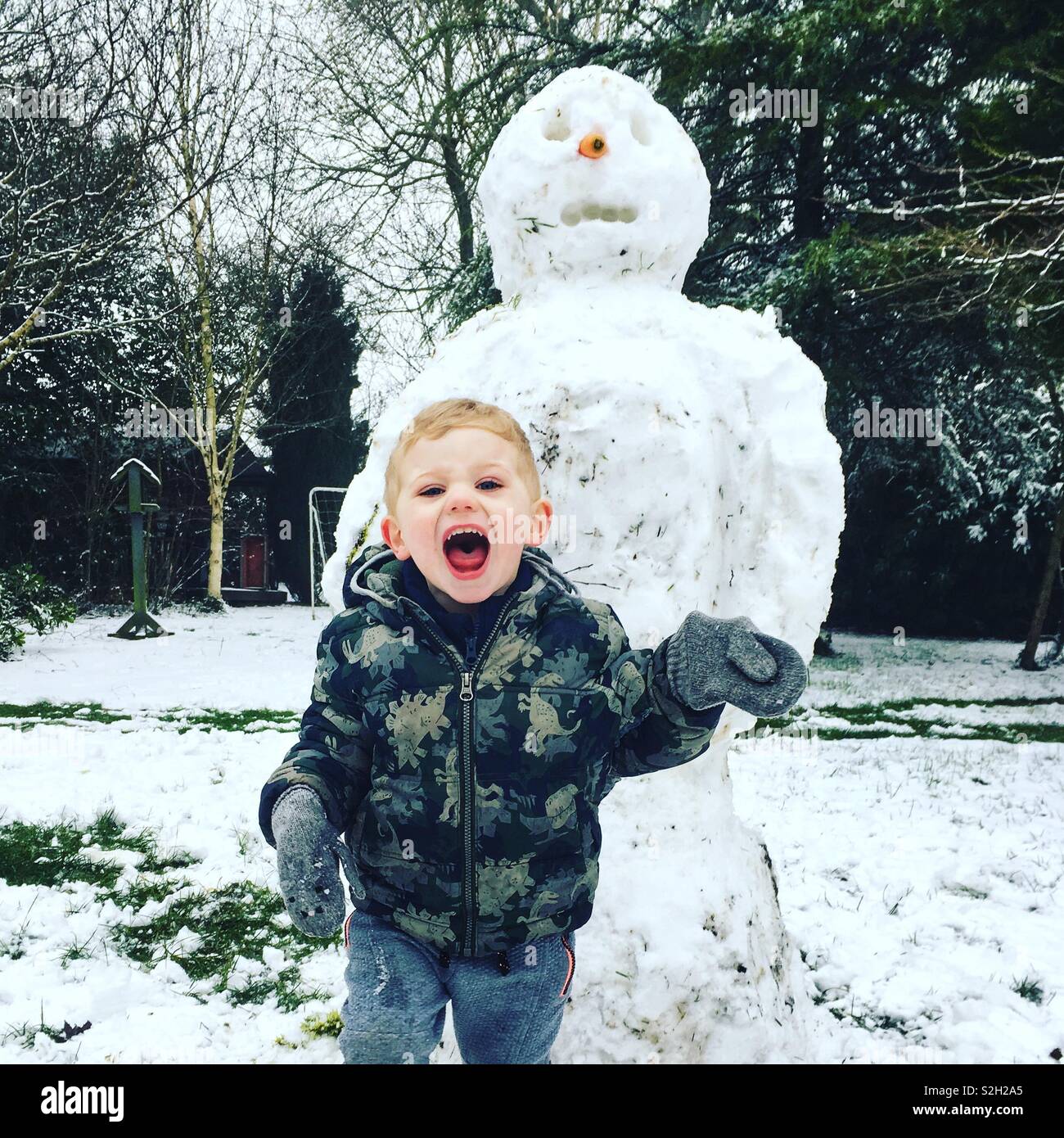 Two year old boy with a large snowman, Hampshire, England, United Kingdom. - Smartphone Captured Stock Image